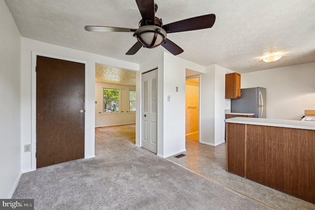 kitchen featuring freestanding refrigerator, a ceiling fan, brown cabinets, a textured ceiling, and baseboards
