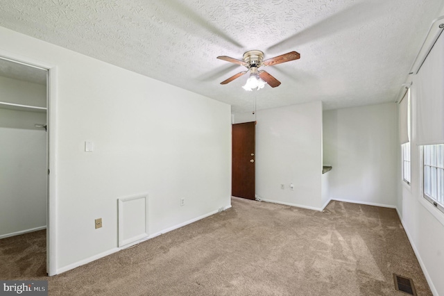 unfurnished bedroom featuring carpet, a walk in closet, a textured ceiling, baseboards, and a ceiling fan