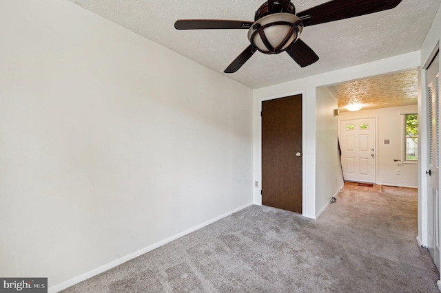 carpeted spare room featuring a textured ceiling, baseboards, and ceiling fan