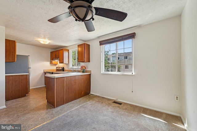 kitchen with brown cabinetry, a peninsula, under cabinet range hood, a textured ceiling, and light countertops