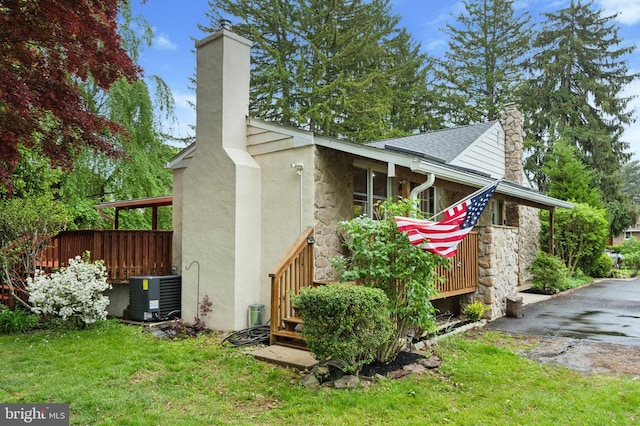 view of side of home with stone siding, stucco siding, a chimney, central AC unit, and a yard