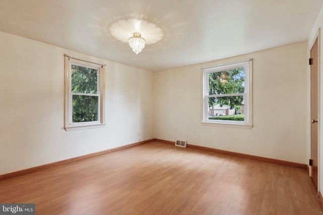 spare room featuring visible vents, light wood-style flooring, baseboards, and a healthy amount of sunlight
