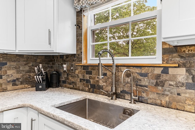 kitchen with a sink, decorative backsplash, light stone countertops, and white cabinets