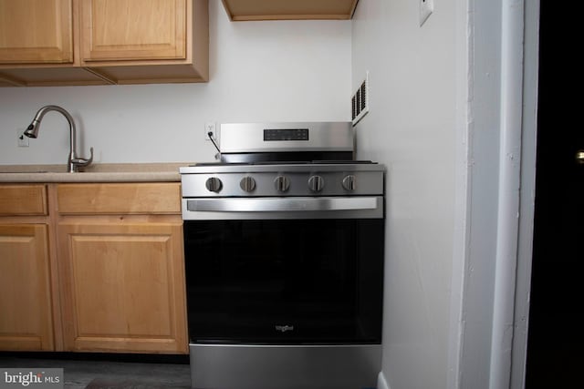 kitchen with stainless steel electric stove, light brown cabinetry, a sink, and light countertops