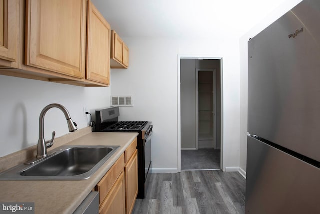 kitchen featuring light brown cabinetry, appliances with stainless steel finishes, a sink, visible vents, and dark wood-style floors