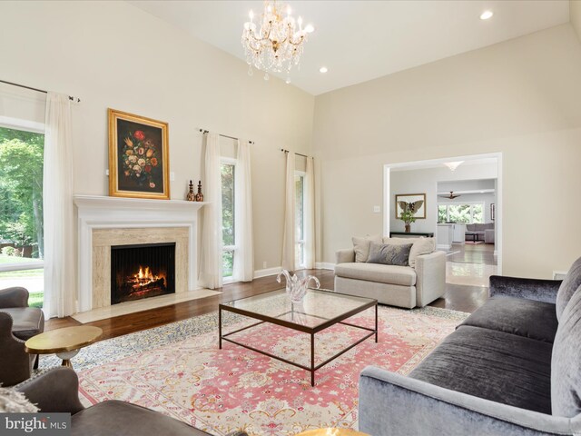 living area featuring wood finished floors, plenty of natural light, a towering ceiling, a premium fireplace, and a chandelier