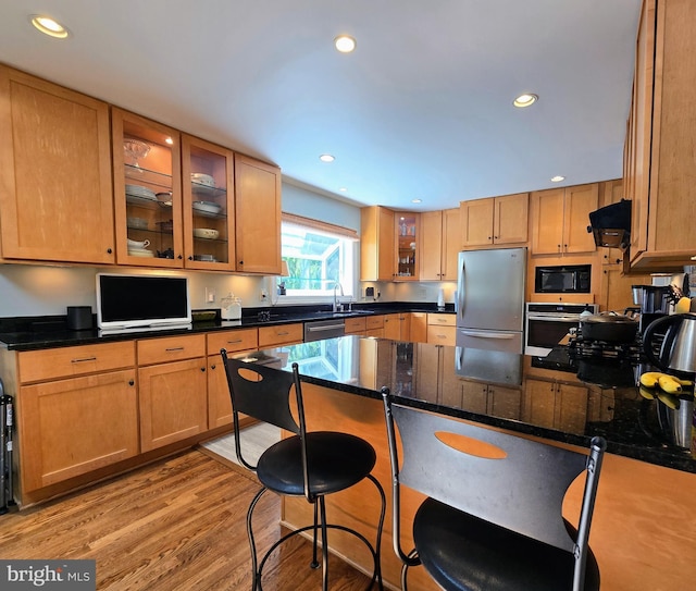 kitchen with appliances with stainless steel finishes, a sink, recessed lighting, a kitchen bar, and glass insert cabinets
