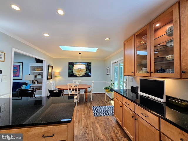 kitchen with crown molding, a skylight, hanging light fixtures, wood finished floors, and glass insert cabinets