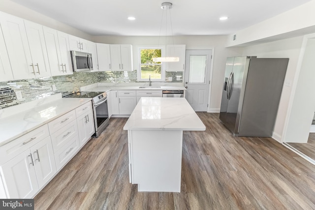 kitchen with a sink, tasteful backsplash, white cabinets, a kitchen island, and appliances with stainless steel finishes