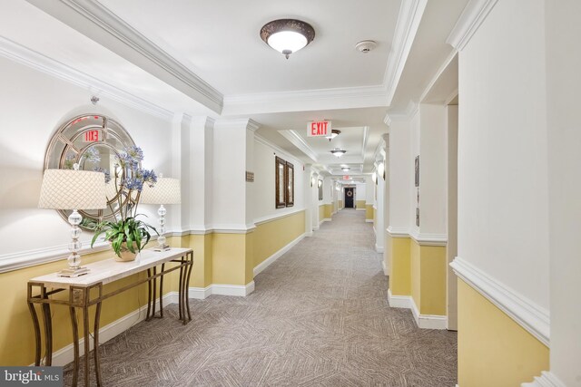 corridor featuring carpet flooring, ornate columns, baseboards, and crown molding