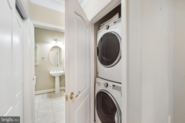 clothes washing area featuring light tile patterned floors, baseboards, stacked washer / dryer, and a sink