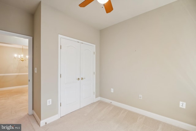 unfurnished bedroom featuring ceiling fan with notable chandelier, baseboards, light carpet, and a closet