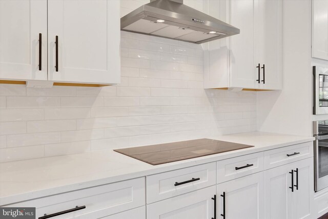 kitchen featuring wall chimney range hood, backsplash, and white cabinets