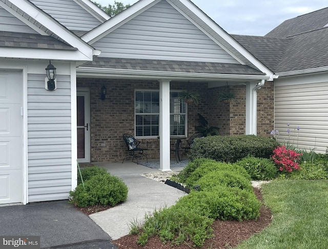 property entrance featuring covered porch, a shingled roof, and brick siding