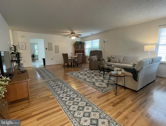 living area featuring baseboards, a ceiling fan, a textured ceiling, and wood finished floors