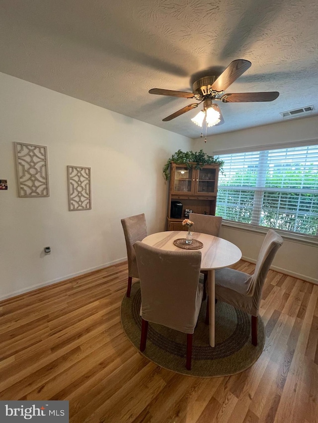 dining room featuring a ceiling fan, a textured ceiling, visible vents, wood finished floors, and baseboards
