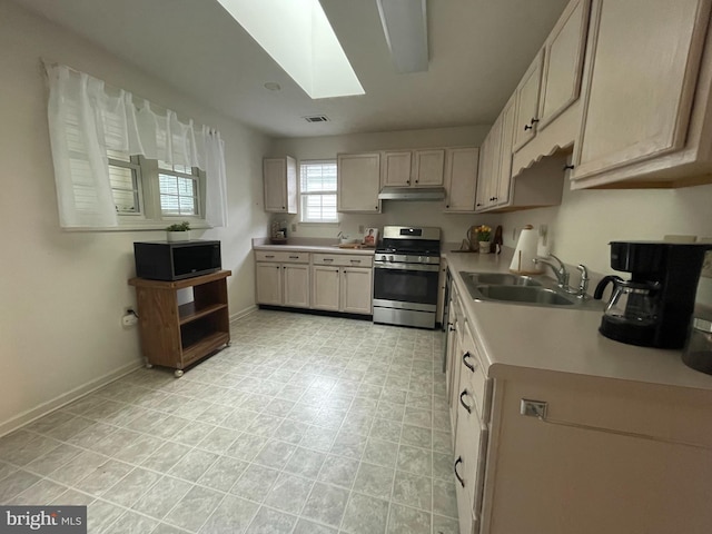 kitchen with light countertops, under cabinet range hood, stainless steel range with gas stovetop, a sink, and a skylight