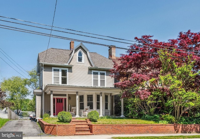 view of front of home with a shingled roof, fence, covered porch, and a chimney