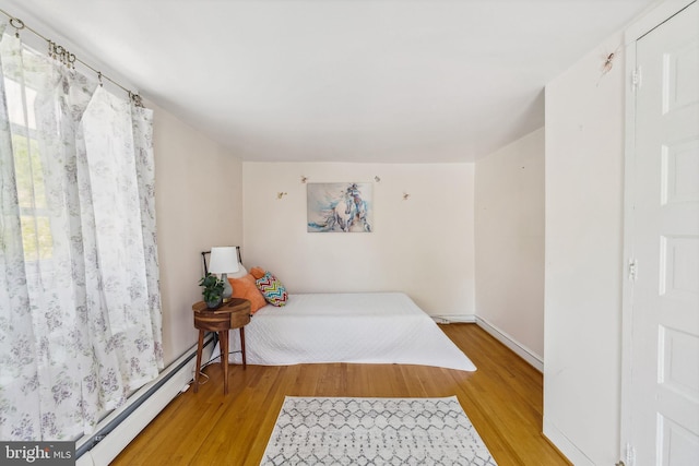 bedroom with baseboards, a baseboard heating unit, and light wood-style floors