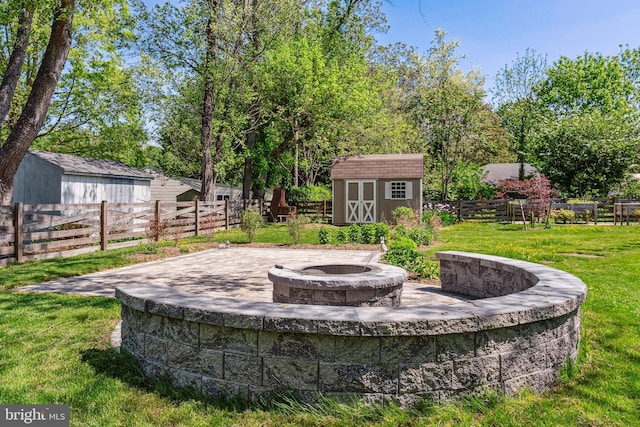 view of yard featuring a fire pit, fence, a shed, a patio area, and an outbuilding