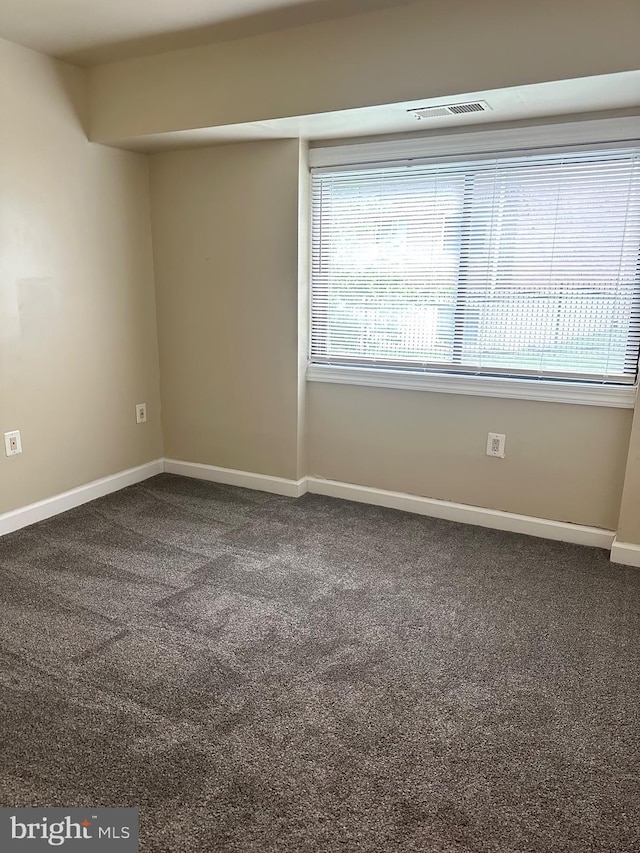 spare room featuring baseboards, dark carpet, and visible vents