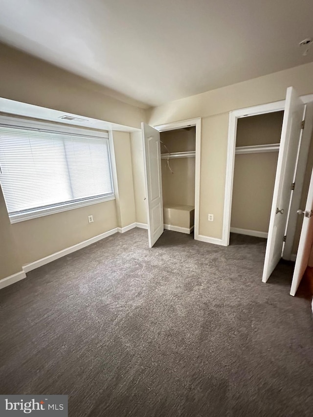 unfurnished bedroom featuring multiple closets, baseboards, and dark colored carpet