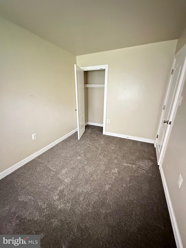 unfurnished bedroom with baseboards, a closet, and dark carpet
