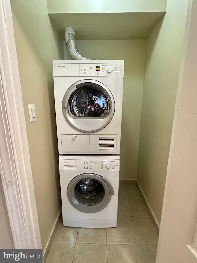 washroom with light tile patterned floors, stacked washer / drying machine, baseboards, and laundry area