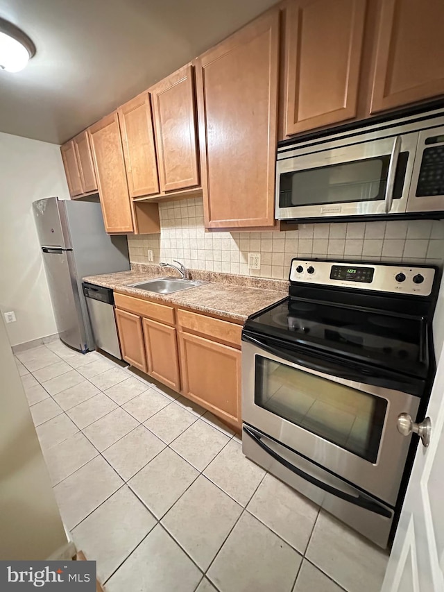 kitchen with a sink, appliances with stainless steel finishes, light tile patterned floors, and backsplash