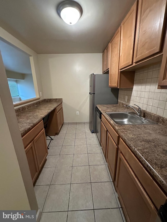 kitchen with dark countertops, a sink, decorative backsplash, light tile patterned floors, and stainless steel dishwasher