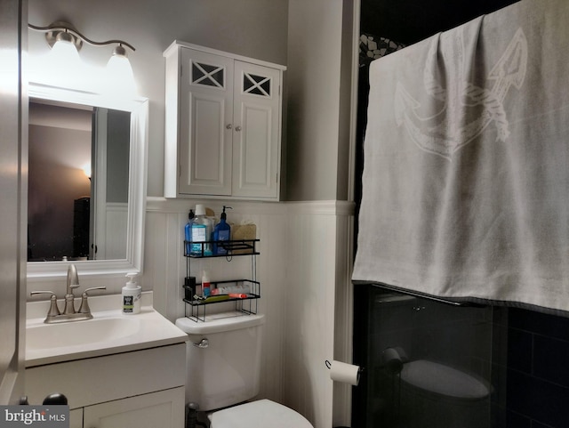 bathroom featuring vanity, wainscoting, a decorative wall, and toilet