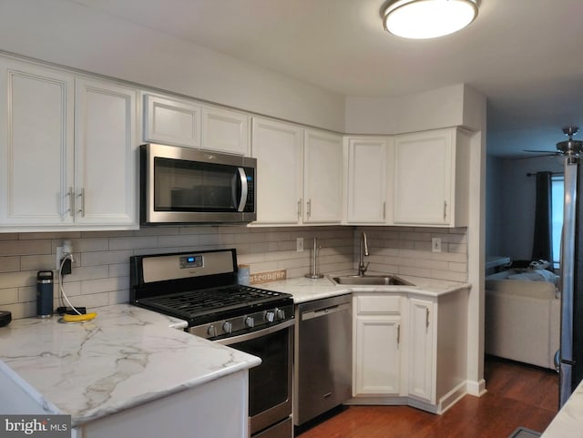 kitchen with decorative backsplash, wood finished floors, white cabinets, a sink, and stainless steel appliances