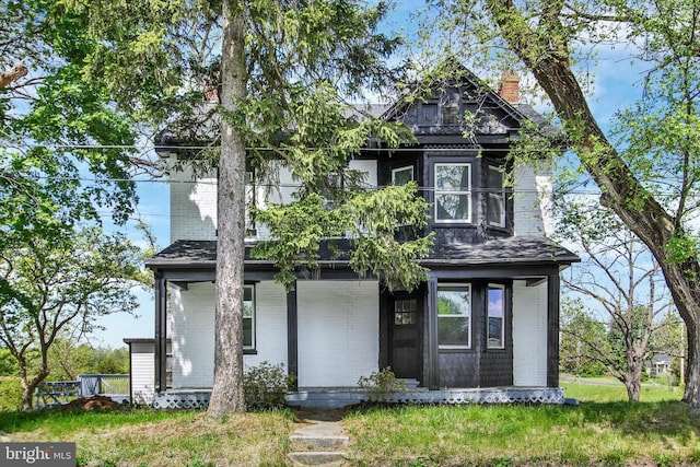 view of front of house featuring a porch, brick siding, and a chimney