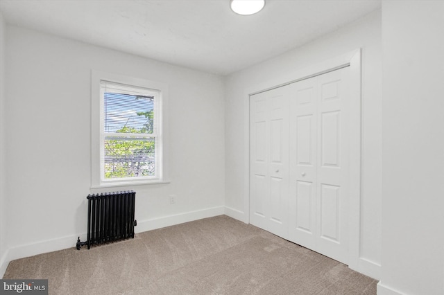 unfurnished bedroom featuring a closet, radiator, baseboards, and carpet flooring
