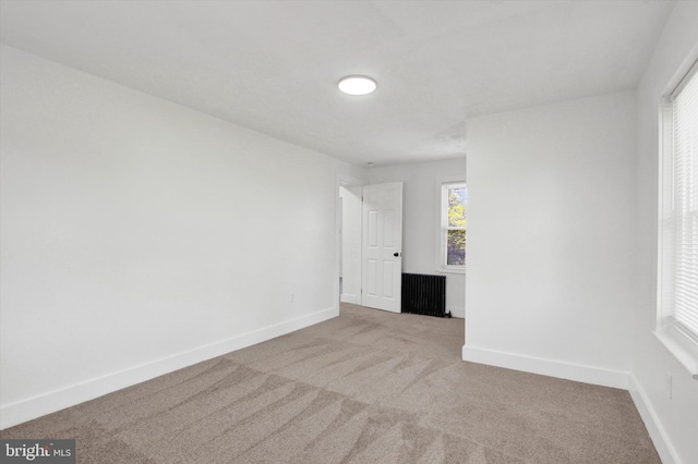 empty room featuring baseboards, radiator heating unit, and carpet