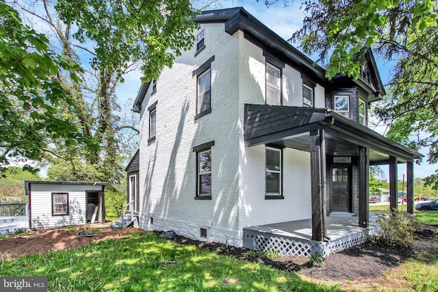 view of side of home featuring covered porch, an outdoor structure, a yard, and brick siding