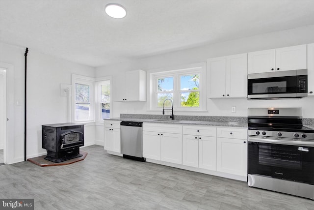 kitchen with a sink, appliances with stainless steel finishes, a wood stove, and white cabinetry