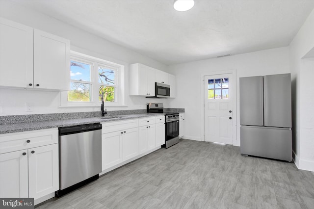 kitchen featuring white cabinetry, appliances with stainless steel finishes, a sink, and light stone counters