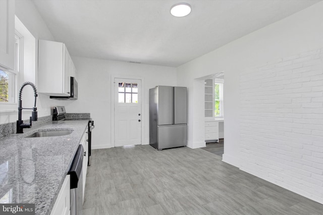 kitchen featuring a sink, white cabinetry, brick wall, and stainless steel appliances