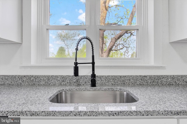 interior details featuring a sink, white cabinets, and light stone countertops
