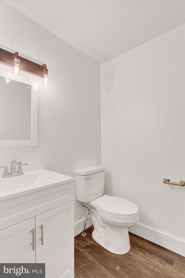 half bath featuring baseboards, wood finished floors, toilet, and vanity