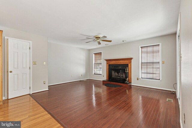 unfurnished living room with ceiling fan, hardwood / wood-style floors, a fireplace with raised hearth, and baseboards