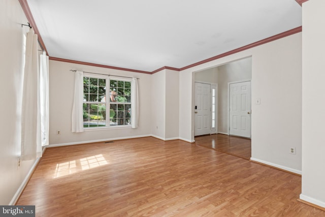 empty room with crown molding, light wood-type flooring, and baseboards
