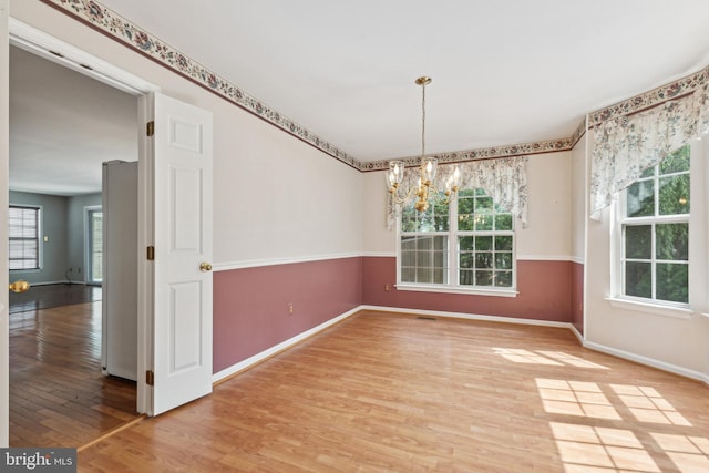 unfurnished dining area featuring light wood-style floors, a chandelier, and baseboards