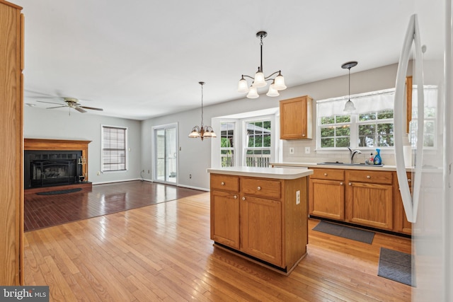 kitchen featuring a chandelier, a sink, light wood-type flooring, a fireplace with raised hearth, and light countertops