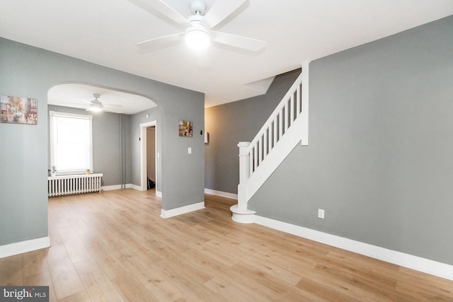 interior space with ceiling fan, arched walkways, radiator, baseboards, and light wood-type flooring