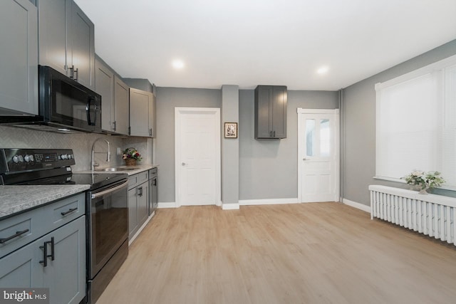 kitchen with electric range, black microwave, a sink, baseboards, and radiator heating unit