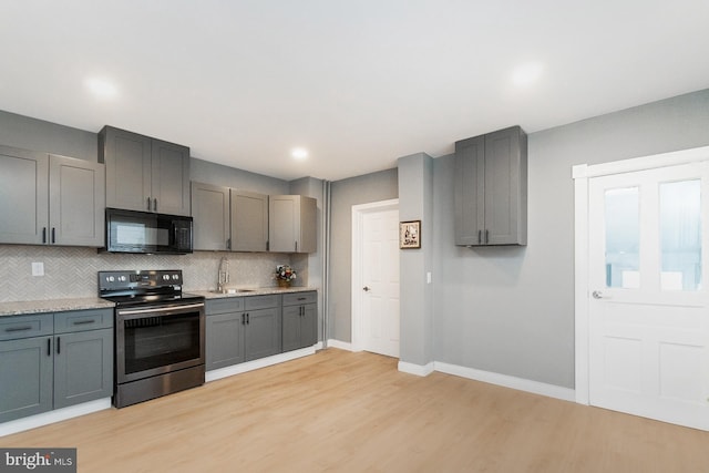 kitchen featuring black microwave, baseboards, decorative backsplash, and stainless steel range with electric cooktop
