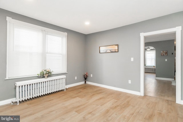 unfurnished room with radiator, baseboards, and wood finished floors