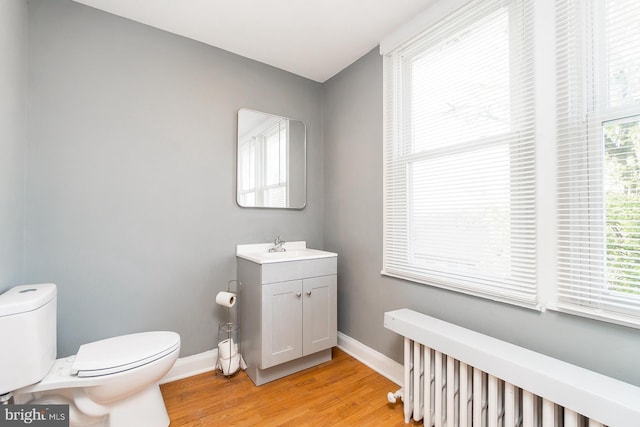 half bathroom with baseboards, wood finished floors, toilet, and vanity